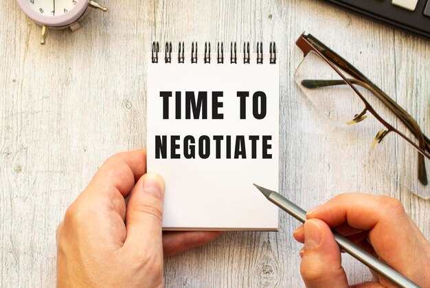 손은 공책에 연필로 TIME TO NEGOTIATE라는 텍스트를 씁니다.