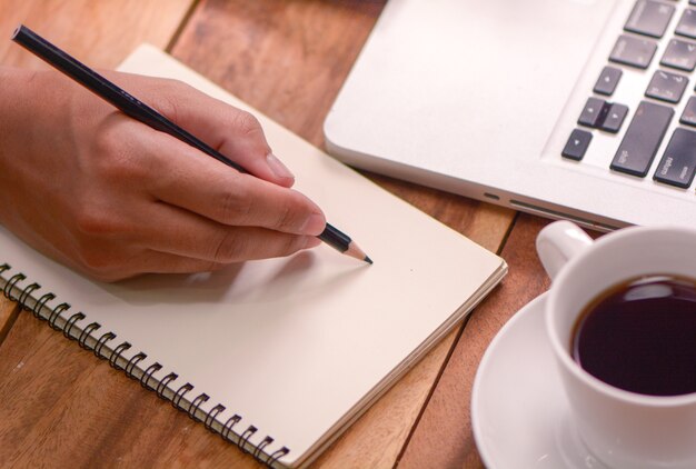 Hand on writing on note paper with coffee and laptop on wood table, working concept