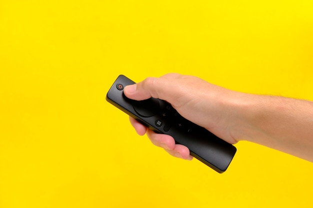 Hand yellow background holds TV remote by pressing button with finger