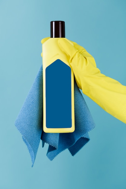 Рука в желтой перчатке держит бутылку лака и синюю тряпку