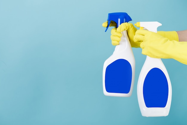 Hand in yellow glove holds spray bottle of liquid detergent on blue background