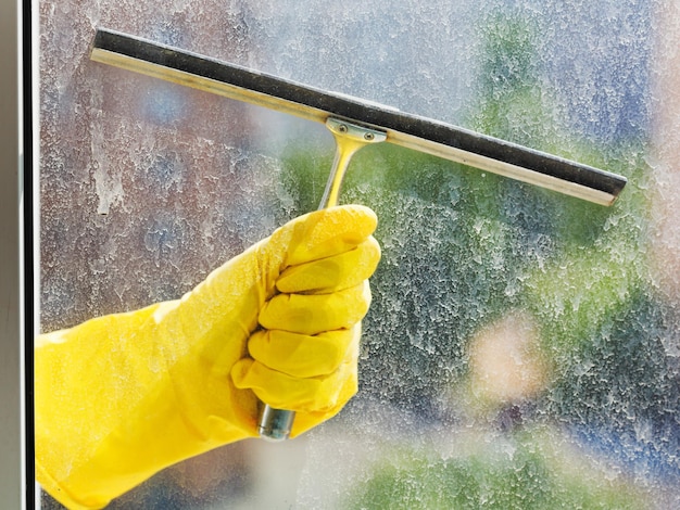 Photo hand in yellow glove washes window by squeegee