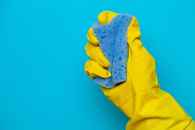 Mano in guanto giallo con straccio su sfondo blu concetto di pulizia.