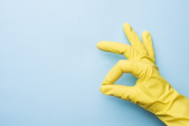 Hand in yellow gloves for cleaning on blue background. 