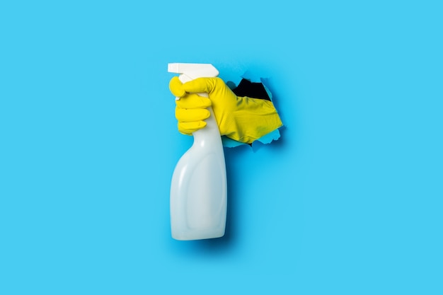 Photo hand in yellow gloves holding spray on a bright blue