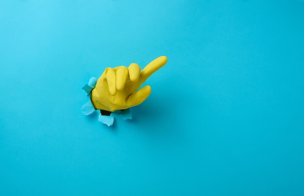 Hand in a yellow latex glove points a finger on a blue background. Place for inscription of discounts, offer or announcement.