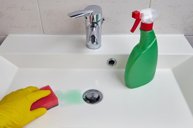 Hand in yellow protective gloves cleans the sink in the bathroom with a sponge and cleaning agent