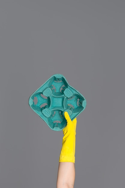 Hand in a yellow rubber glove for cleaning holds a green cardboard 