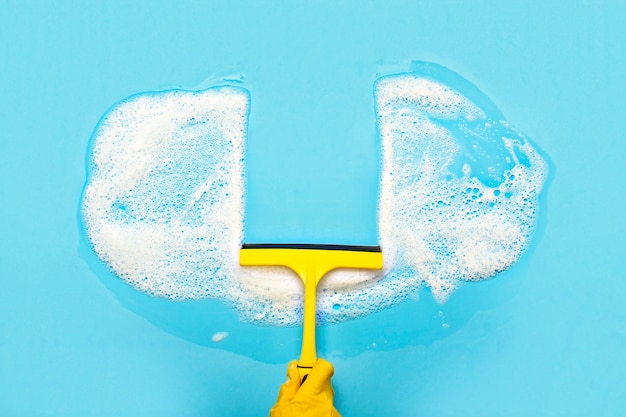 Hand in a yellow rubber glove holds a scraper for cleaning and wipes soap