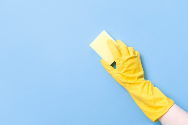 Photo hand in a yellow rubber glove holds a yellow sponge for washing dishes and cleaning