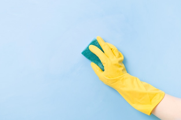 A hand in a yellow rubber glove holds a yellow sponge with a green rough side for cleaning complex dirt