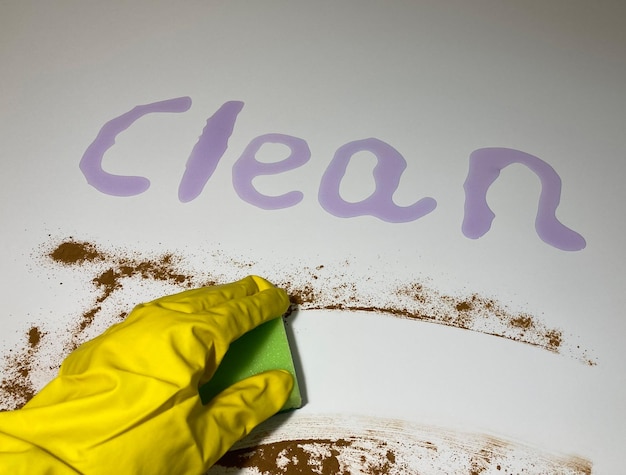 A hand in a yellow rubber glove, wipes the dirt off the white table with a green washcloth