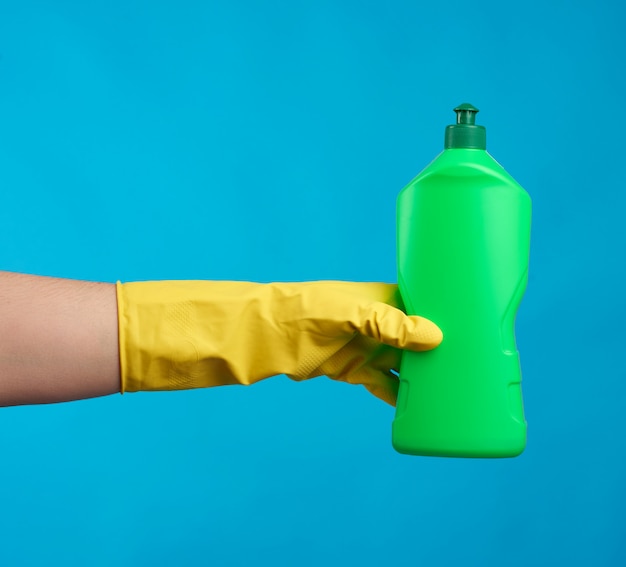 Hand in yellow rubber gloves holds a green plastic bottle