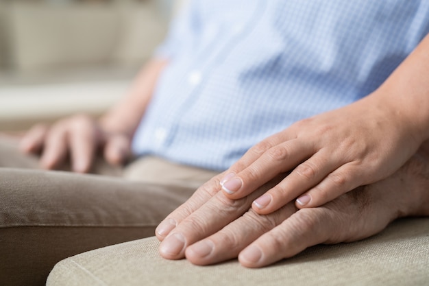 Hand of young affectionate and careful woman on that of her senior father on handle of beige soft couch