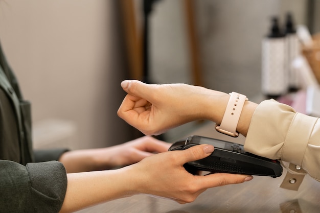 Hand of young contemporary female customer with smartwatch keeping her wrist over pos terminal during contactless payment