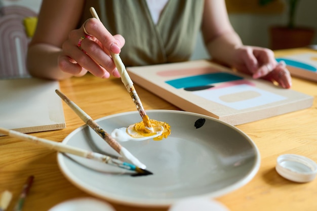 Hand of young creative female mixing white and yellow colors on plate