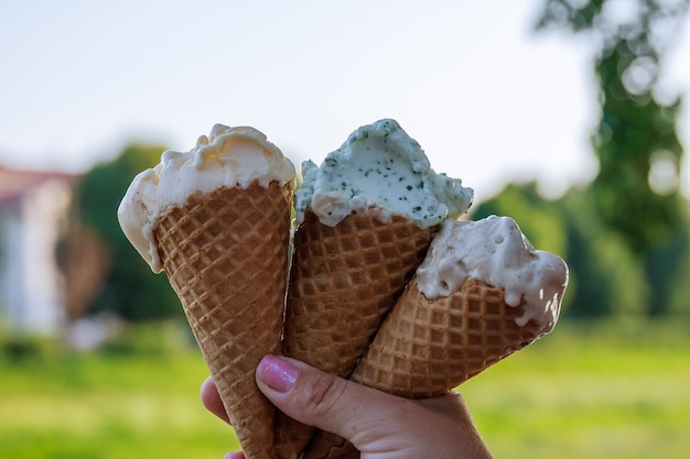 The hand of a young girl holds three ice creams in waffle cone.