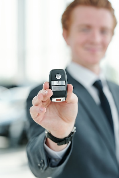 Foto mano di un giovane manager o venditore di veicoli in possesso di un sistema di allarme telecomandato durante la vendita di una nuova auto a uno dei clienti nel centro auto