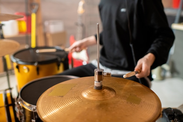 Hand of young musician in black hoodie holding drumstick over cymbals