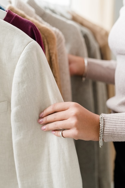 Hand of young woman holding by sleeve of white jacket from new seasonal collection in casualwear department