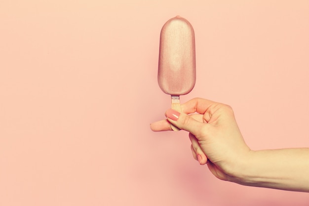 Hand of young woman holding ice cream on pink background. Fashion Background. Summer Concept. Toning.