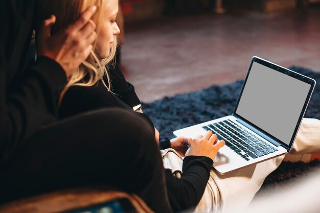 Photo hand of a young woman working at laptop at home while sitting on the floor leaning on her boyfriend.