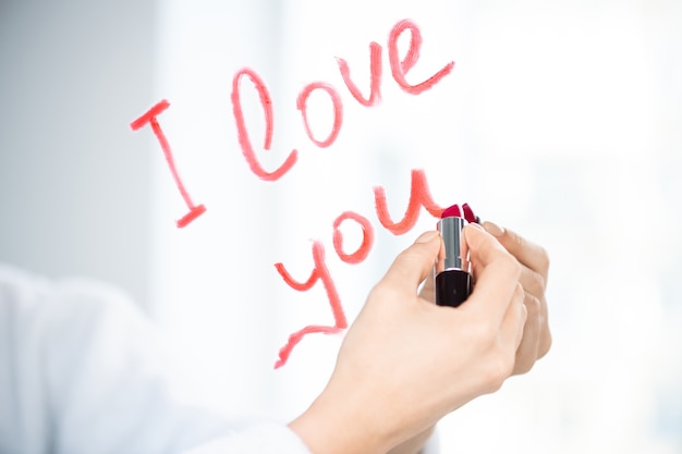 Hand of young woman writing love message with red or crimson lipstick on mirror in the morning