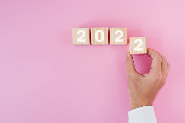 Hand zet een kubieke houten blok met de tekst 2022, start en trend, kalender en tijd, doel van het definiëren en plannen van prestatie, motivatie en ambities, bedrijfsconcepten.