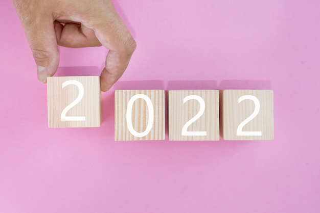 Hand zet een kubieke houten blok met de tekst 2022, start en trend, kalender en tijd, doel van het definiëren en plannen van prestatie, motivatie en ambities, bedrijfsconcepten.