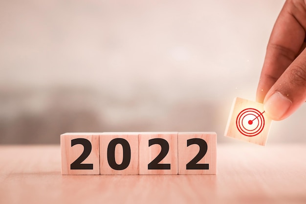 hand zet houten kubussen met Nieuwjaar 2022 en doelpictogram. Concept voor succes in het toekomstige doel en het verstrijken van de tijd. Gelukkig nieuwjaar.