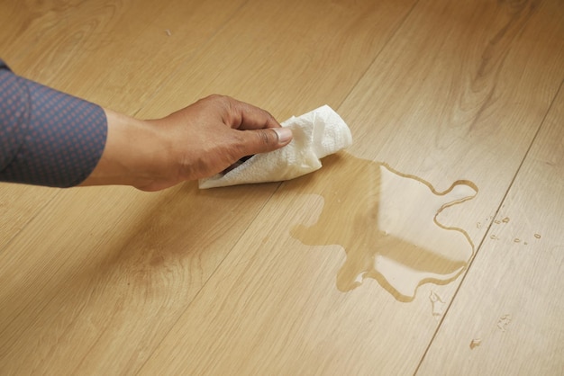 Handafvegen van gemorste thee met papieren servet op de vloer