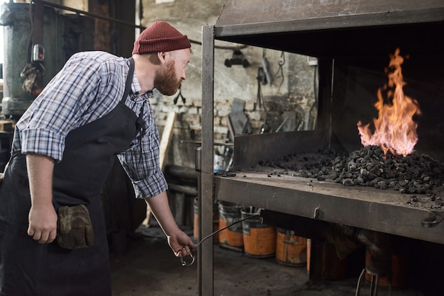 Handarbeider die de steenkool gebruikt om het vuur in de oven te verbranden tijdens zijn werk in de fabriek