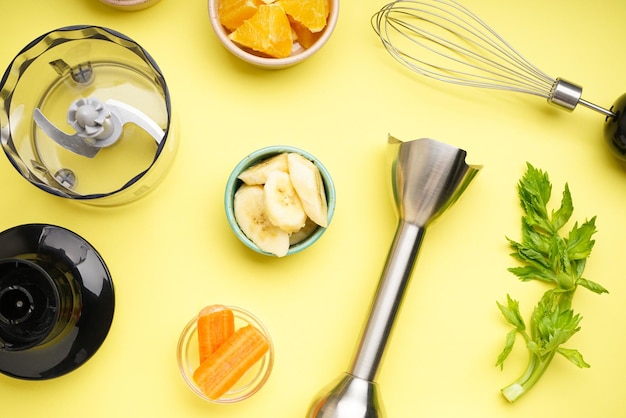 Handblender en accessoires met gesneden fruit op een gele achtergrond, close-up. Plat leggen.