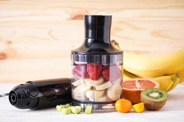 Handblender en accessoires met gesneden fruit op een houten ondergrond. Detailopname.