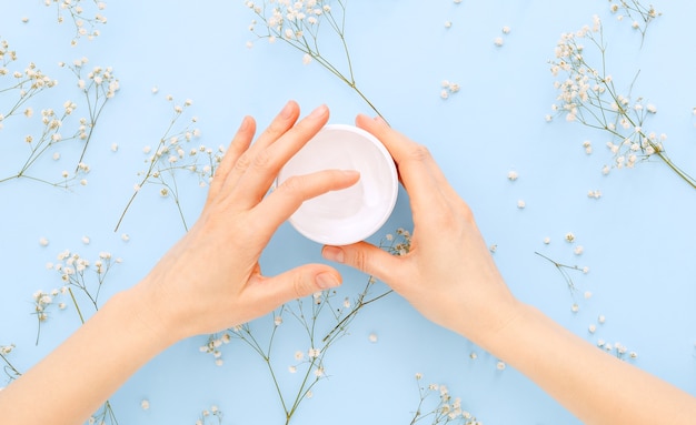 Handcrème, vrouwelijke handen biologische natuurlijke crème cosmetica toe te passen op een pastel blauw gekleurde achtergrond. huidverzorgingscrème in potje voor handen, lichaam.