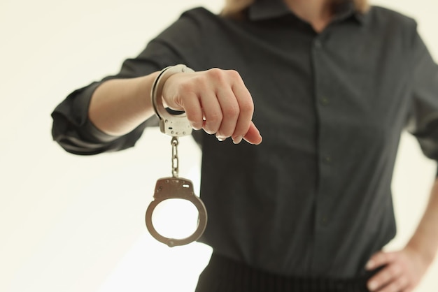 Handcuffs hanging on wrist of woman standing on beige background female person in dark shirt