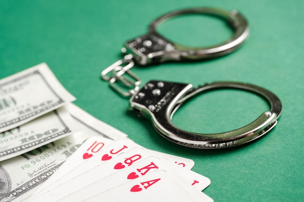 Handcuffs lie next to playing cards and US dollars on a green background