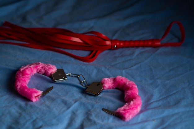 Photo handcuffs with red fur and a whip devices for love games on the bed