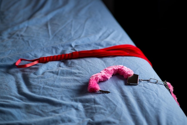 Photo handcuffs with red fur and a whip devices for love games on the bed