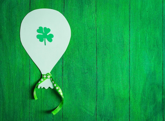 A handcut paper ball with a ribbon and a clover leaf on it lies on the left on a green homemade wooden background with copy space for your text on the right flat lay closeupPatrick's day concept