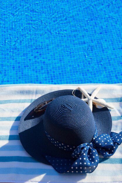 Handdoek en zomer blauwe hoed met schelpen bij het zwembad, kopieer ruimte op blauw water