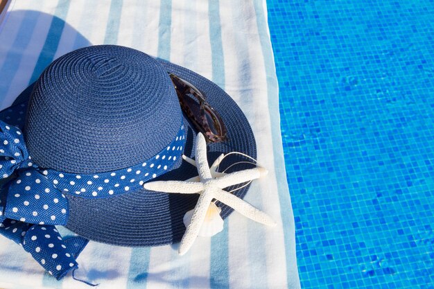 Handdoek en zomerhoed met schelpen in de buurt van water van het zwembad