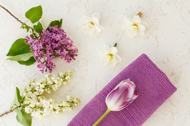 Handdoek, toppen van narcissen bloemen, tulp en lila bloemen op de witte gestructureerde achtergrond. Bovenaanzicht.