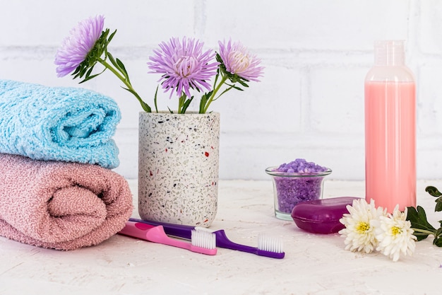 Handdoeken, een blikje met zeezout, een fles shampoo, tandenborstels, zeep en bloemen van asters op een witte ondergrond