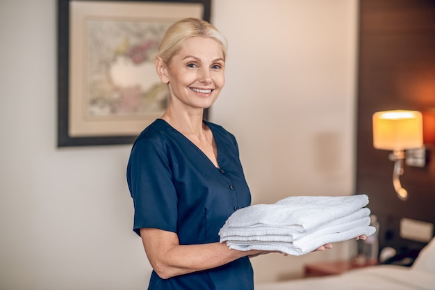 Handdoeken wisselen. Dienstvrouw in donkerblauw uniform met schone handdoeken