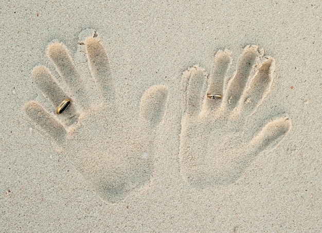 Foto handdruk van paar met trouwringen op zand