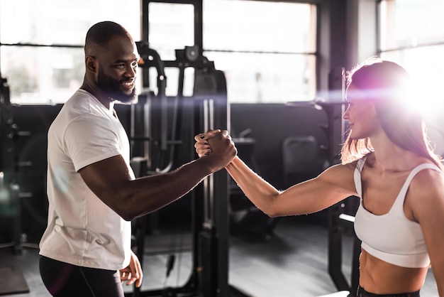 Handdruk van sportieve Afrikaanse man met vrouw groet partner oefening workout bij fitness gym