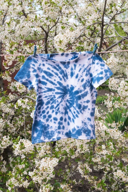 A handdyed tie dyestyle Tshirt in blue is drying against the background of a flowering tree