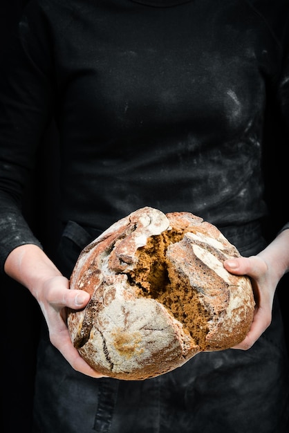 Handen breken zwart brood van meel Zwarte kookachtergrond Geïsoleerd op zwarte achtergrond