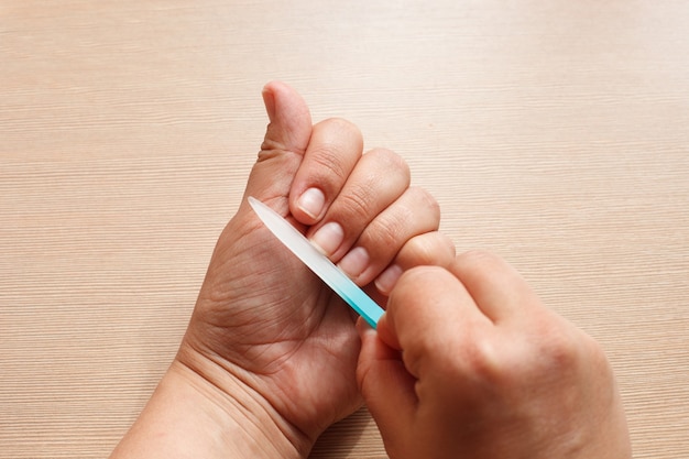 Handen close-up, een meisje doet een manicure aan zichzelf, blauwe nagelvijl.